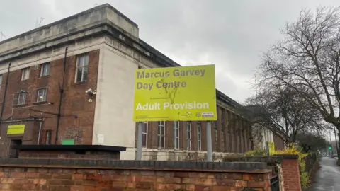 Street level image of a large red brick building with a sign for the Marcus Garvey Day Centre in the foreground