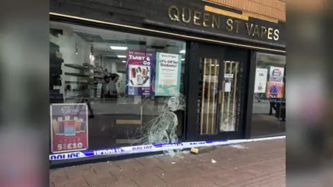 The outside of the Queen Street Vapes shop with a broken window and police tape in front of it