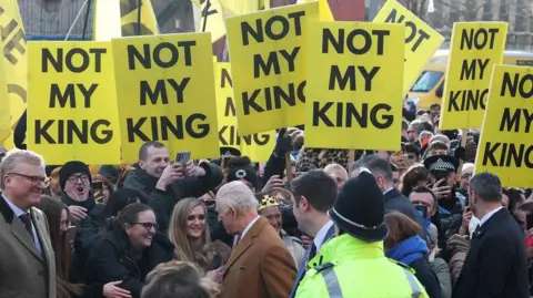 Reuters King Charles greeting the crowd of people at Centre Square. Large, yellow placards that read 'NOT MY KING' are being held up and cover the top of the photo.