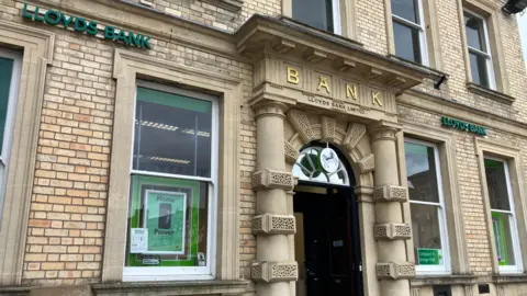 A large beige brick building with two Lloyds Bank signs at the top and Bank written in gold lettering over the main entrance.