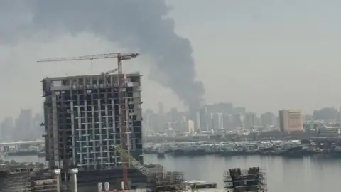 Alfie Chenery Plumes of grey smoke rise high up into the sky from the city's skyscrapers behind the port