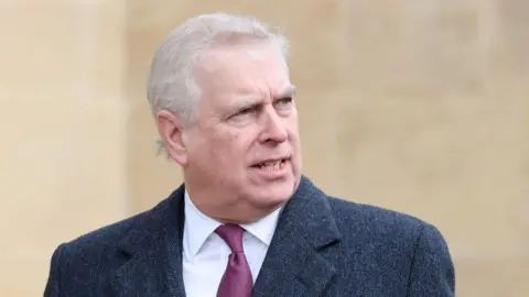 Getty Images Prince Andrew, is a middle-aged man with grey hair. He is wearing a dark grey coat and red and blue patterned tie with a white shirt. He is looking off camera to his left