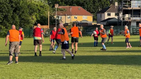Walking rugby players in brightly coloured orange and red bibs, passing a ball along the line and trying to score.