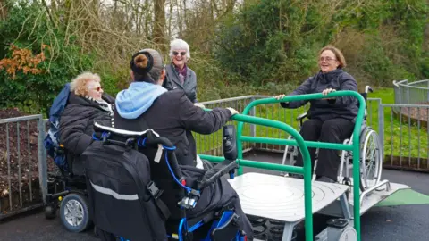 Salisbury City Council Four people, three in wheelchairs, smile widely in a park