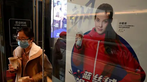 Getty Images A woman walk past a poster showing China's US-born gold medallist Eileen Gu