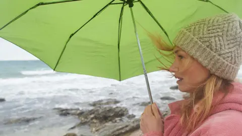 Getty Images A woman with an umbrella by the sea - stock photo