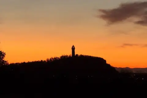 Paul Weir Wallace Monument - tall narrow structure - silhouetted against an orange morning sky.