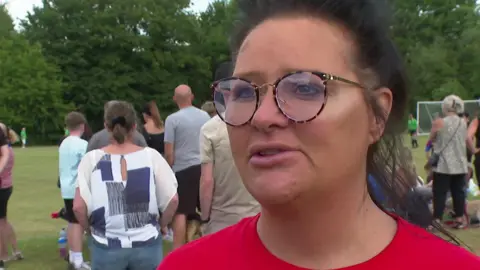 A woman with tied up black hair wears a red T shirt and round glasses. She is looking beyond the camera. Her mouth is slightly open.