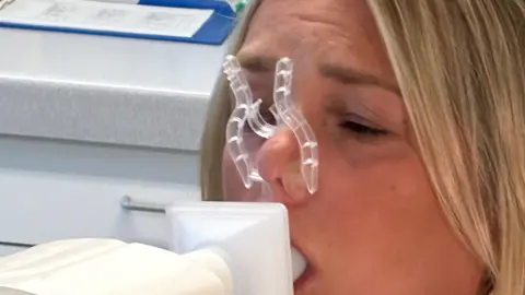 Helen blowing into a lung function machine at Nottingham's Queen's Medical Centre. A plastic clip on her nose helps her force more air through her mouth during the health check