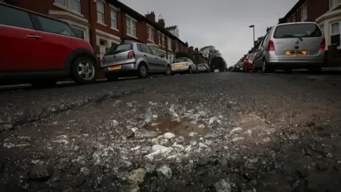A pothole viewed on the ground Osborne Road in Jesmond. Cars are in the background.
