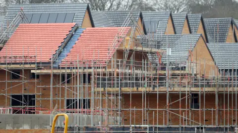 A number of homes in a row at an under-construction housing development. Scaffolding has been set up in the foreground.
