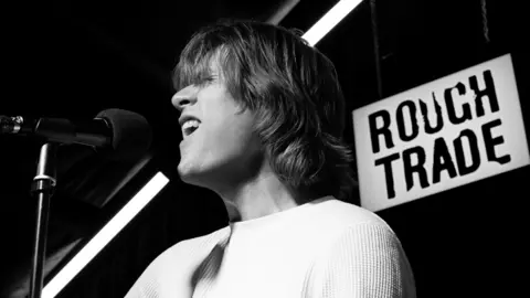 Jess Greaves Matt Thomson singing at Rough Trade Nottingham. He has medium length hair and wears a white top.