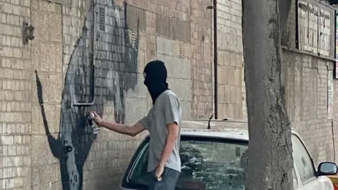 Man spray painting Banksy rhino artwork