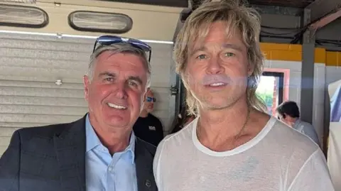 Martin Donnelly Martin Donnelly (left) a man with grey hair and glasses on his head, wearing a dark jacket and blue shirt. Alongside him is Brad Pitt, a man with blond hair, wearing a white T-shirt.