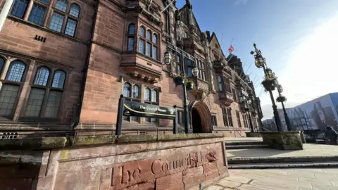 The headquarters of Coventry City Council, an ornate sandstone building with lead lined windows, is pictured. It shows signage which reads "The Council House"