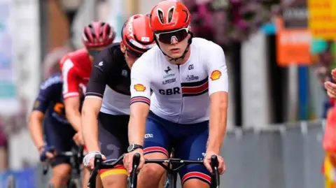 Vanessa Barrow A young man on a three wheeled bike cycling on cobbled roads.