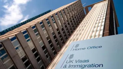 A tall rise building with a sign in front of it saying 'Home Office' and 'UK Visas & Immigration'