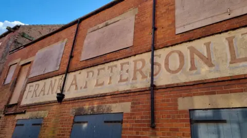 Ellen Hunter A derelict brick building with the sign Frank A Peterson on the front. Windows on the second tier are boarded up. There are blue wooden doors on the bottom level