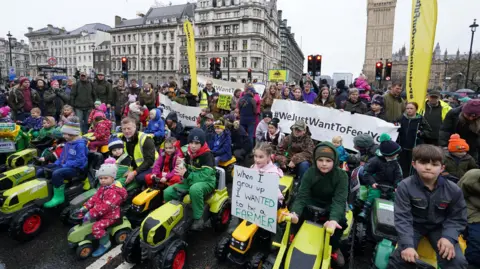 PA Dozens of children sit on toy tractors in central London, at the protest eiqkiqtriqrrinv