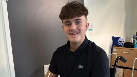 Family Handout A teenage boy in a dark blue polo shirt in a hospital room looking at the camera and smiling.