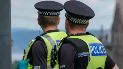 Getty Images The back of two Police Scotland officers wearing their recognisable fluorescent yellow padded vests and black checked hats 