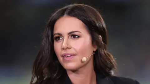 A close-up of a dark haired woman looks off camera with a microphone mouthpiece coming out from behind her ear