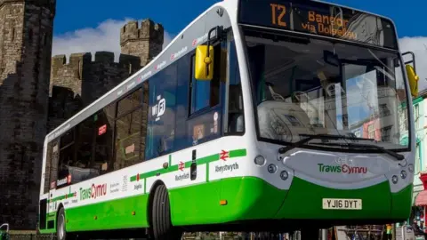 Welsh Government A TrawsCymru bus, whose sign says it is the T2 to Bangor via Dolgellau, pictured in front of a castle.