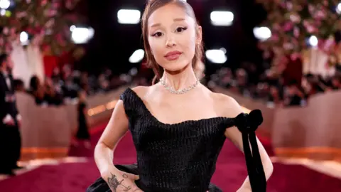 Ariana Grande appears on a red carpet in January wearing a black dress.