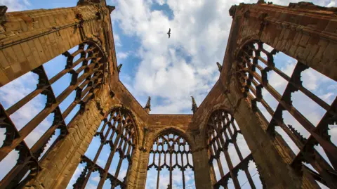 Getty Images A bird flies high above the stone ruins of the cathedral