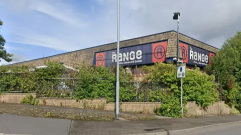 Google Maps The outside of The Range home, leisure and garden store with a fence around the property covered in greenery and a pavement on the other side of the fence.