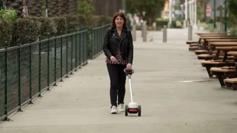 Emma Tracey uses a Glide - a device with two wheels and a long handle - on a walkway