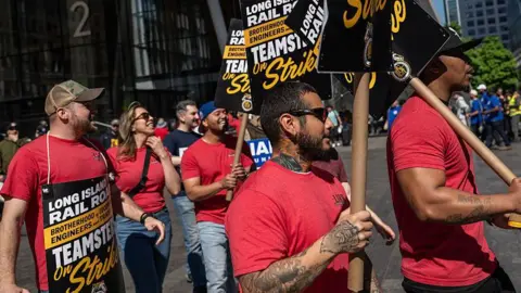 line of picketing workers holding up signs announcing a strike in front of NYC skyscraper