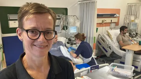Nicola Alderson stood in the Anthony Nolan Cell Collection Centre at Nottingham's Queens' Medical Centre. She is the charity's Chief Operating Officer. Behind her two donors are giving stem cells to be sent off for transplant to unrelated recipients