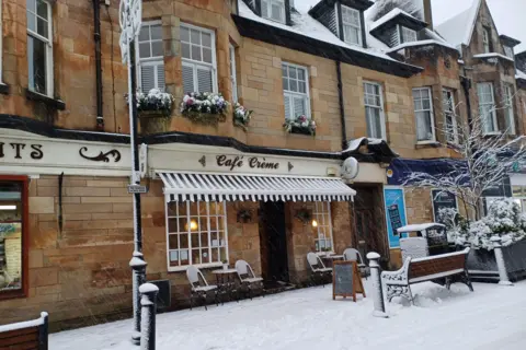 Sandy Welsh There are tables and chairs covered in snow outside a cafe building.