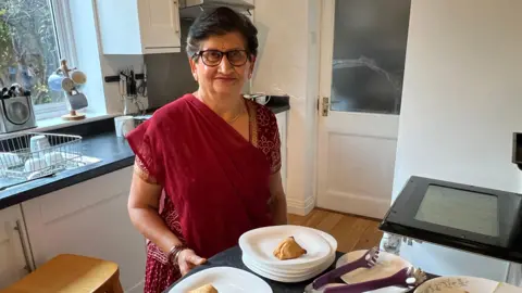 A woman in a red sari standing in a kitchen with samosas in front of her