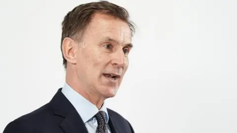 PA Media Jeremy Hunt is talking and looking to the right of the picture. He is wearing a pale blue shirt, tie and dark coloured suit.