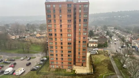 Simon Thake/BBC A birds eye view of a tall red brick tower block overlooking grey streets 
