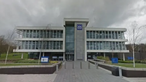 Durham Police headquarters. The building is made of grey stone and has two upper floors made up of many windows.