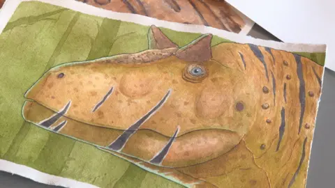 Lee Brown A vibrant watercolour painting of a dinosaur with brown skin and stripes across its mouth stares out of the canvas. But it is not threatening. It is posed in a calm and thoughtful way.