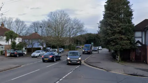 A suburban road with trees and grey cars. 