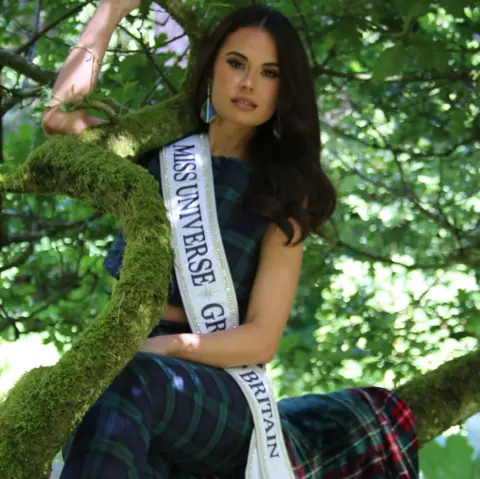 Danielle Latimer Miss Universe GB Christina Chalk sitting in a tree wearing a tartan suit