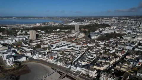 BBC A drone shot of Jersey. There is a blue sky, and the sea is in the background.