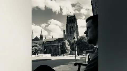 Adam Powell Dr Adam Powell, wearing glasses, looks to the left of the camera as he is sitting outside. Behind him is Durham Cathedral