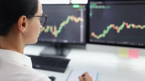 Stock image of woman looking at screens showing financial markets information