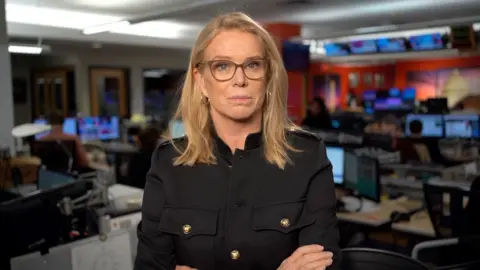 Katty Kay wearing a achromatic  overgarment   with her arms folded