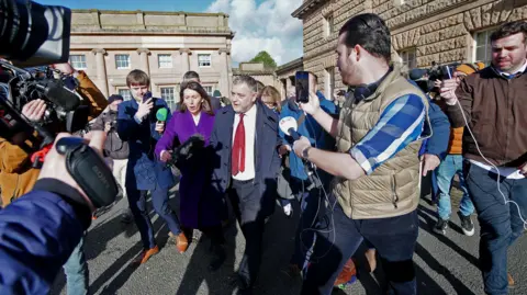 PA Mike Amesbury, wearing a dark suit with a white shirt and red tie, is surrounded by reporters as he leaves Chester Crown Court.