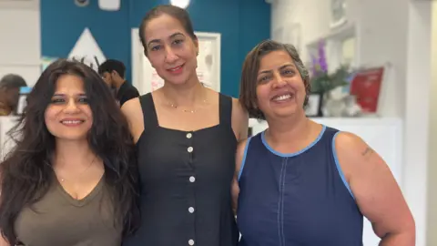 Three women smile widely inside a building.