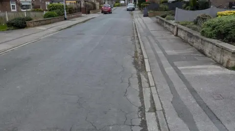 A residential street with an empty road. In the far distance are two cars.