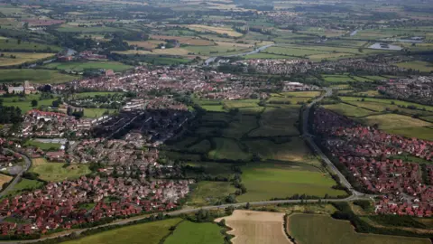 An aerial shot of Tewkesbury in Gloucestershire showing housing and major roads as well as the countryside surrounding the town