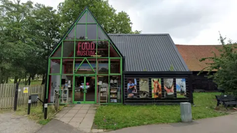 Exterior of the Food Museum showing a glass fronted triangular building surrounded by fencing and grass